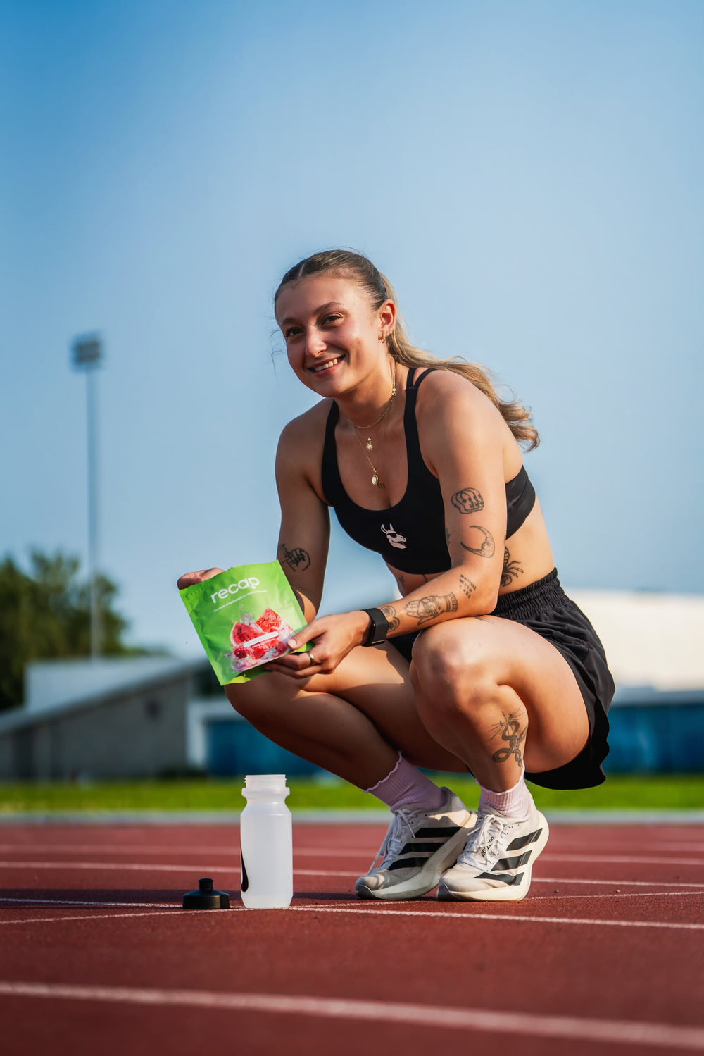 Une femme sur une piste d’athlétisme avec un sachet Recap Framboise-Melon et sa bouteille.