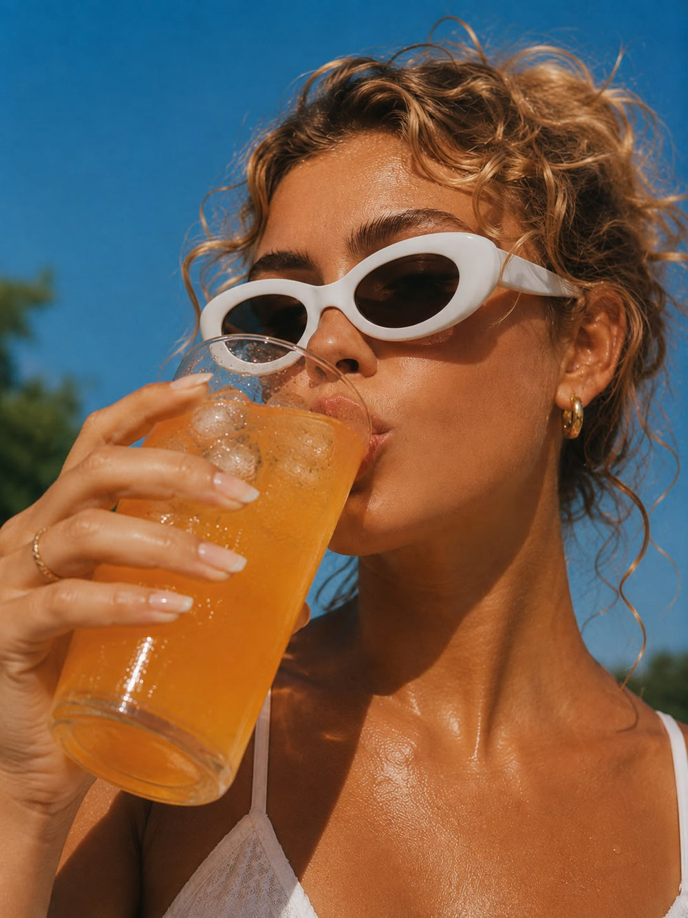 Une femme en lunettes de soleil savoure une boisson orange bien fraîche à l’extérieur.