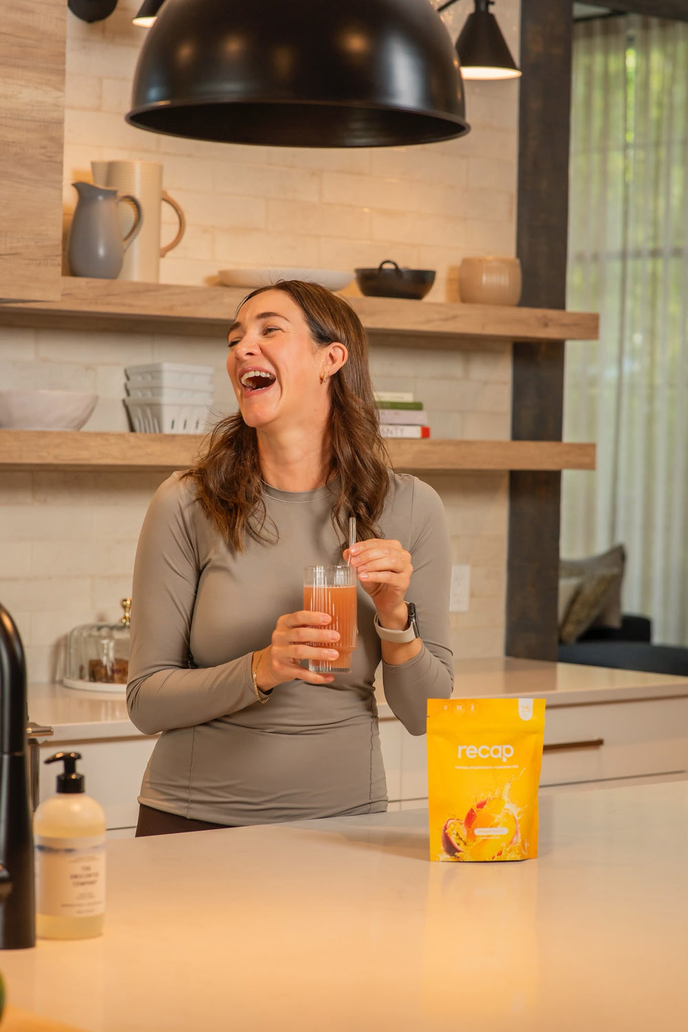 Une femme savoure une boisson Recap dans sa cuisine, avec le sachet Mangue-Passion sur le comptoir.