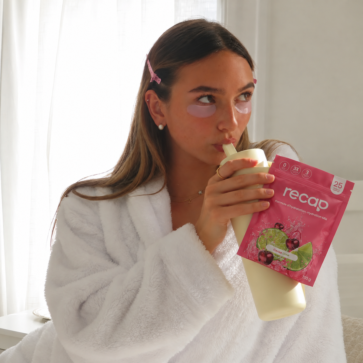 Une femme en peignoir tient un sachet Recap Cerise Lime et boit dans son gobelet.